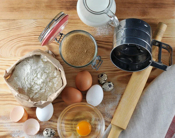 Pişirme için ayarlayın. Resimde, süt, un, bıldırcın yumurtası ve yumurta, bir oklava, bir un elemek, bir kase protein ile bir sarısı ve bir yumurta kabuğu bir sürahi. Ahşap arka plan. Close. Yukarıdan görüntüle.