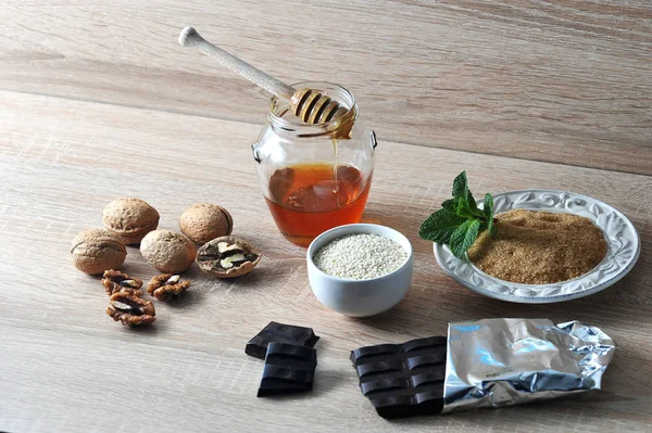 A set for making a useful dessert. In the frame honey, cane sugar, sesame, mint, dark chocolate, walnuts for making sweets in home conditions. Light background. Close-up.