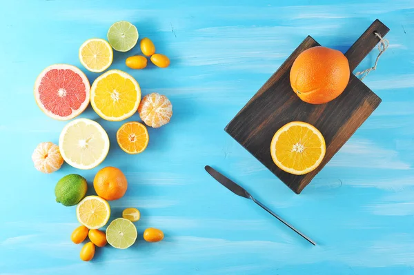 Narenciye bileşimi. Çerçevede portakal, mandalina, limon, limon, kumquat, pembe ve sarı greyfurt. Tahta tahtanın yanında bir portakal ve yarım portakal var. Mavi ahşap arka plan. Yukarıdan görüntüle