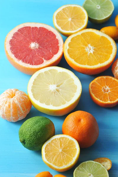 Çeşitli narenciye. Çerçevede, kireç, kumquat, kabuğuz mandalina, portakal, mandalina, limon, greyfurt, kireç yarıları. Mavi ahşap arka plan. Close. Çerçevenin dikey yönü.