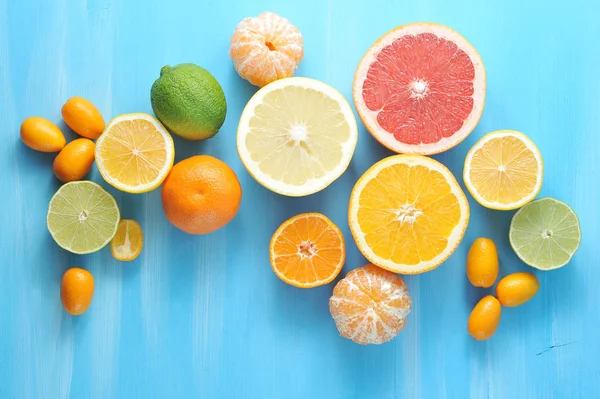 Narenciye kolajı. Çerçevede, kireç, kumquat, kabuğuz mandalina, portakal, mandalina, limon, greyfurt, kireç yarıları. Mavi ahşap arka plan. Close. Yukarıdan görüntüle.