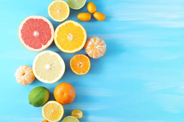 Çeşitli narenciye. Çerçevede, kireç, kumquat, kabuğuz mandalina, portakal, mandalina, limon, greyfurt, kireç yarıları. Mavi ahşap arka plan. Close. Yukarıdan görüntüle.