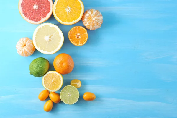 Çeşitli narenciye. Çerçevede, kireç, kumquat, kabuğuz mandalina, portakal, mandalina, limon, greyfurt, kireç yarıları. Mavi ahşap arka plan. Close. Yukarıdan görüntüle.