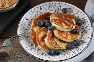 Tabakta küçük krepler. Iştah açıcı krepler yaban mersini ile dekore edilmiştir. Bir sonraki çatal. Kaba ahşap arka plan. Close. Makro fotoğrafçılık.