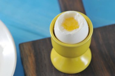 Özel bir fincan yumuşak bir kapta Yumurta. Fincan koyu ahşap bir tahta üzerinde duruyor. Kabuğun bir kısmı kayıp ve sarısı görünüyor. Mavi ahşap arka plan. Close. Makro fotoğrafçılık.