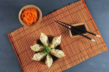 Damping - farklı dolgular ile ince bir hamur bir tabak. Tabağın altında bambudan yapılmış bir peçete var. Soya sosu ve yemek çubuklarına yakın. Close. Makro fotoğrafçılık. Yukarıdan görüntüle. 