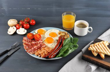İngiliz kahvaltısı - brunch. Bir tabak kızarmış pastırma, sosis, kızarmış taze domates ve champignons, domates soslu beyaz fasulye, tost, kızarmış yumurta. Çerçevede, bir bardak portakal suyu ve kahve..