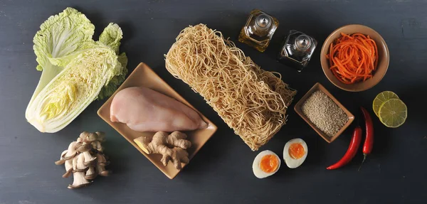 Bir wok erişte pişirmek için bir set. Çerçevede, buğday erişte, tavuk, Çin lahanası, istiridye mantarı, baharatlı havuç, kireç, susam, zencefil kökü, biber. Close. Yukarıdan görüntüle.