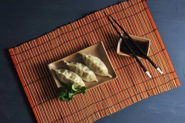 Damping - farklı dolgular ile ince bir hamur bir tabak. Tabağın altında bambudan yapılmış bir peçete var. Soya sosu ve yemek çubuklarına yakın. Close. Makro fotoğrafçılık. Yukarıdan görüntüle.