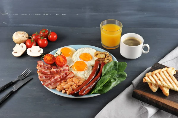İngiliz kahvaltısı - brunch. Bir tabak kızarmış pastırma, sosis, kızarmış taze domates ve champignons, domates soslu beyaz fasulye, tost, kızarmış yumurta. Çerçevede, bir bardak portakal suyu ve kahve..