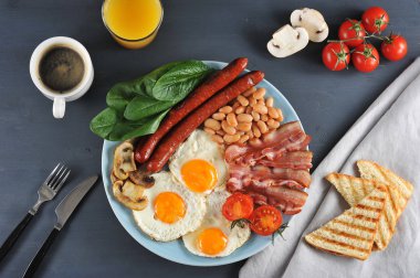 İngiliz kahvaltısı - brunch. Bir tabak kızarmış pastırma, sosis, kızarmış taze domates ve champignons, domates soslu beyaz fasulye, tost, kızarmış yumurta. Portakal suyu ve kahveye yakın. Yukarıdan görüntüle.