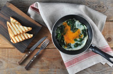 Tavada ıspanak ile çırpılmış yumurta. Beyaz ekmek ve çatal bıçak takımının bir sonraki tostu. Ahşap arka plan. Yukarıdan görüntüle.