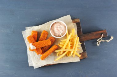 Balık, tahta bir tahtanın üzerine ekmek yapıyor. Patates kızartması ve bir fincan sosun yanında. Koyu ahşap arka plan. Close. Yukarıdan görüntüle.