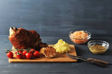 Çek ve Alman mutfağından geleneksel bir yemek. Fırında domuz eklemi. Kiraz domates, patates püresi, ızgara sarımsak. Hardal, lahana turşusu, çatal bıçak takımı çerçevesinde. Koyu ahşap arka plan. Close.