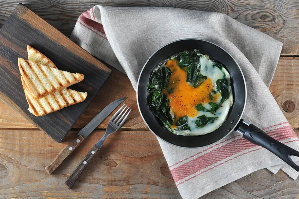 Tavada ıspanak ile çırpılmış yumurta. Beyaz ekmek ve çatal bıçak takımının bir sonraki tostu. Ahşap arka plan. Yukarıdan görüntüle.