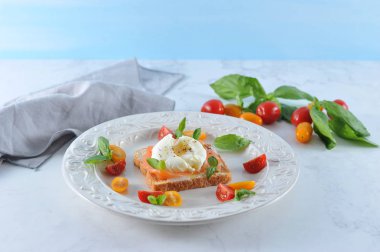 Tuzlu somon ve yumurta ile tost bir tabakta haşlanmış. Çanak çok renkli kiraz domates ve fesleğen yaprakları ile dekore edilmiştir. Açık arka plan. Close. Çerçevenin dikey yönü.