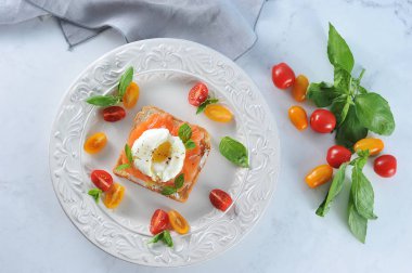 Tuzlu somon ve yumurta ile tost bir tabakta haşlanmış. Çanak çok renkli kiraz domates ve fesleğen yaprakları ile dekore edilmiştir. Açık arka plan. Close. Yukarıdan görüntüle. 