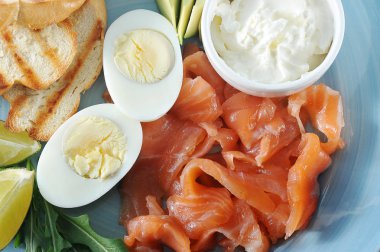 Kırmızı tuzlu balık, tost, haşlanmış yumurta, yumuşak krem peynir, mavi bir tabakta kireç dilimleri. Açık arka plan. Yukarıdan görüntüleyin. Close. Makro fotoğrafçılık.