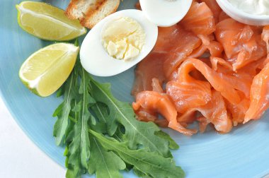 Kırmızı tuzlu balık, tost, haşlanmış yumurta, arugula, yumuşak krem peynir, mavi bir tabakta kireç dilimleri. Açık arka plan. Yukarıdan görüntüleyin. Close. Makro 