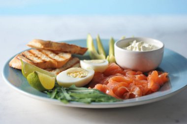 Kırmızı tuzlu balık, tost, haşlanmış yumurta, arugula, yumuşak krem peynir, mavi bir tabakta kireç ve avokado dilimleri. Brunch için ayarlayın. Açık arka plan. Close. Makro fotoğrafçılık.