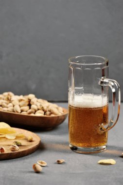 Bir bardak hafif bira. Bir kase de bira antep fıstığı ve bir taella patates cipsi için bir aperatif olarak. Gri ahşap arka plan. Close. Çerçevenin dikey yönü.