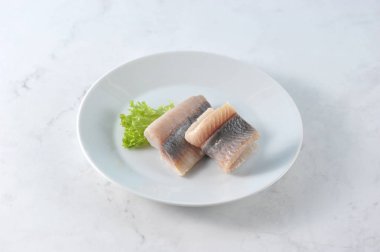 Beyaz bir tabakta Atlantik ringa filetosu. Balık marul bir yaprak ile dekore edilmiştir. Açık mermer arka plan. Close. Yukarıdan görüntüle.