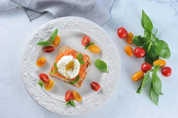 Tuzlu somon ve yumurta ile tost bir tabakta haşlanmış. Çanak çok renkli kiraz domates ve fesleğen yaprakları ile dekore edilmiştir. Açık arka plan. Close. Yukarıdan görüntüle. 
