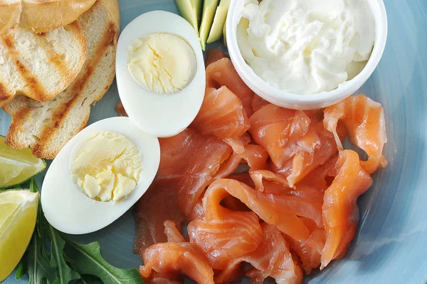 Kırmızı tuzlu balık, tost, haşlanmış yumurta, yumuşak krem peynir, mavi bir tabakta kireç dilimleri. Açık arka plan. Yukarıdan görüntüleyin. Close. Makro fotoğrafçılık.