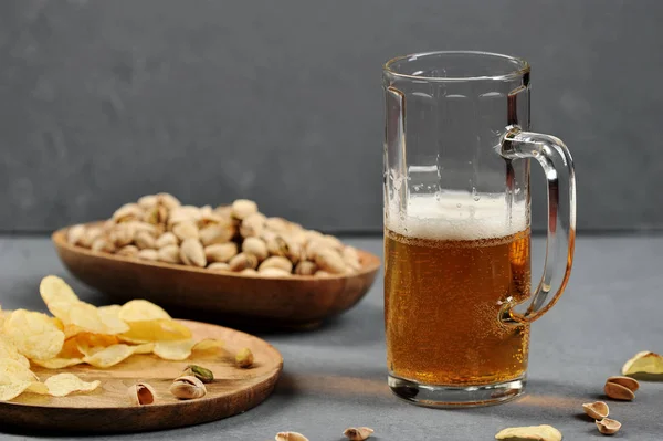 Bir bardak hafif bira. Bir kase de bira antep fıstığı ve bir taella patates cipsi için bir aperatif olarak. Gri ahşap arka plan. Close. 