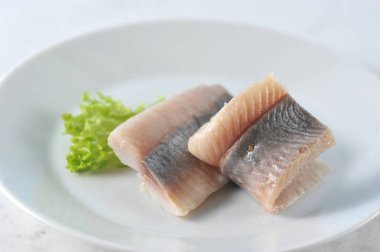 Beyaz bir tabakta Atlantik ringa filetosu. Balık marul bir yaprak ile dekore edilmiştir. Açık mermer arka plan. Close. Makro fotoğrafçılık.