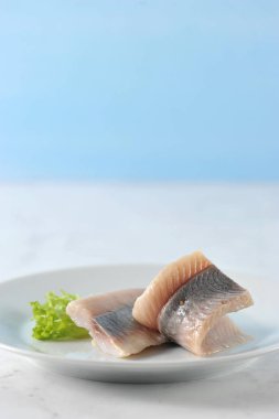 Beyaz bir tabakta Atlantik ringa filetosu. Balık marul bir yaprak ile dekore edilmiştir. Açık mermer arka plan. Close. Makro fotoğrafçılık.