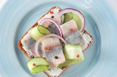 Mavi tabakta ringa balığı olan bir sandviç. Siyah ekmek krem peynir, genç ringa balığı, taze salatalık, soğan halkaları, kırmızı ve karabiber. Yukarıdan görüntüleyin. Close. Makro fotoğrafçılık.