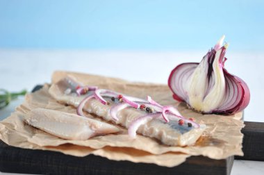 Kağıt üzerinde Atlantik ringa filetosu ve kesme tahtası. Balık üzerinde kırmızı soğan ve biber yarım halkalar vardır. Sonraki yarıya soğan, marul. Açık mermer arka plan. Close. Makro fotoğrafçılık