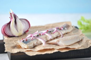 Kağıt üzerinde Atlantik ringa filetosu ve kesme tahtası. Balık üzerinde kırmızı soğan ve biber yarım halkalar vardır. Sonraki yarıya soğan, dereotu. Açık mermer arka plan. Close. 