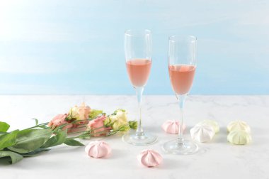 Pembe şaraplı iki bardak. Yüzeydeki çerçevede, çiçekler ve bezeler açık pembe renk şeması içinde yayılır. Açık arka plan. Close.