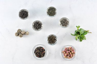 Çeşitli çay. Çerçevesiyah büyük yaprak çay, yeşil, süt oolong, aromalı çay, topları çay. Nane taze, gül kurutulmuş tomurcukları. Açık arka plan. Yukarıdan görüntüleyin. Close.