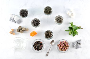 Çeşitli çay ve çaydanlık. Çerçevesiyah büyük yaprak çay, yeşil, yasemin ile yeşil, sütlü oolong, aromalı, topları çay. Nane yaprakları, kurutulmuş çiçek tomurcukları, şeker, çay poşetleri. Yukarıdan görüntüle. 