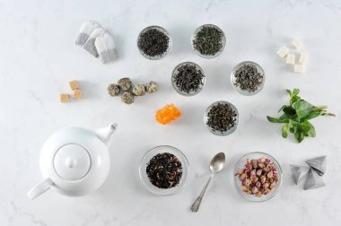  Çeşitli çay ve çaydanlık. Çerçevesiyah büyük yaprak çay, yeşil, yasemin ile yeşil, sütlü oolong, aromalı, topları çay. Nane yaprakları, kurutulmuş çiçek tomurcukları, şeker, çay poşetleri. Yukarıdan görüntüle. 