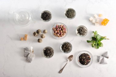 Çeşitli çay ve çaydanlık. Çerçevesiyah büyük yaprak çay, yeşil, yasemin ile yeşil, sütlü oolong, aromalı, topları çay. Nane yaprakları, kurutulmuş çiçek tomurcukları, şeker, çay poşetleri. Yukarıdan görüntüle. 