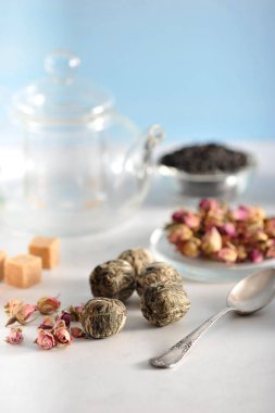 Çay demlemek için bir çaydanlık, kurutulmuş gül tomurcukları, toplarda yeşil çay, şeker kamışı. Çerçevede, bir çay kaşığı. Arka planda siyah çay. Açık arka plan. Close. Makro fotoğrafçılık.