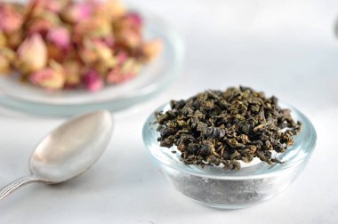 Çay yeşil sütlü oolong. Kurutulmuş gül tomurcuklarının yanında. Çerçevede, bir çay kaşığı. Açık arka plan. Close. Makro fotoğrafçılık.
