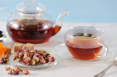 Siyah çaylı çaydanlık ve bir fincan çay. Cam eşyalar. Tabağın yanında kurutulmuş gül tomurcukları vardır, çay demlemek için kullanılır. Açık arka plan. Close.