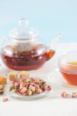 Su ısıtıcısında siyah çay, bir fincan çay, kurutulmuş gül goncası, şeker kamışı. Çerçevede, bir çay kaşığı. Açık arka plan. Close. Makro fotoğrafçılık.