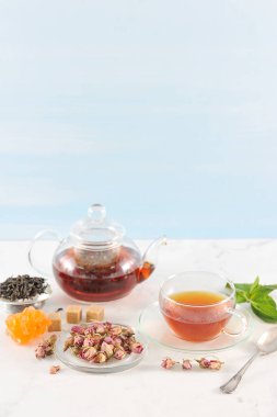 Siyah çaylı çaydanlık ve bir fincan çay. Cam eşyalar. Tabağın yanında kurutulmuş gül tomurcukları vardır, çay demlemek için kullanılır. Çerçeve, kaynak, nane, baston ve kristal şeker. Açık arka plan. Close.