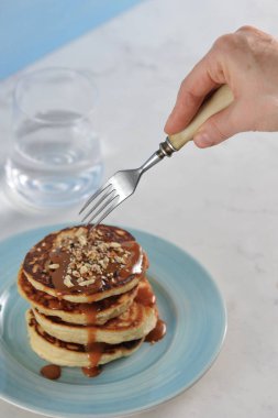 Krepler birbiri üzerine serilir, karamel sos ile dökülür ve rendelenmiş badem serpilir. Krepüzerinde bir çatal ile el getirdi. Çerçevenin dikey yönü. Açık arka plan.