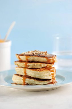 Karamel ve fındıklı krep. Krep bir yığın ile kaplı, karamel şurubu ile dökülür, fındık kırıntıları serpilir. Su dolu bardağın yanında. Close. Çerçevenin dikey yönü.