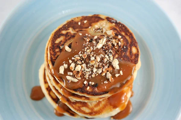 Karamel ve fındıklı krep. Birkaç krep bir yığın ile kaplı, karamel şurubu ile dökülür, hindistan cevizi badem serpilir. Close. Makro çekim. Bir plakanın mavi arka planı.