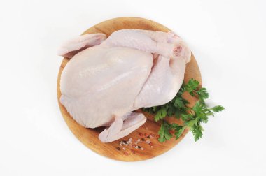 Yuvarlak ahşap bir tahta üzerinde tavuk karkas çiğ. Tavuğun yanındaki tahtada maydanoz ve baharatların yeşili vardır. Beyaz arka plan. Close. Yukarıdan görüntüle.