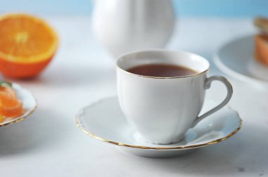 Bir fincan siyah çay ve bir tabak. Çerçevede bir tabak, bir çaydanlık ve yarım portakal var. Açık arka plan. Close. Makro fotoğrafçılık.