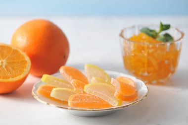 Bir tabakta portakal ve limon dilimleri şeklinde marmelat ve vazoda portakal reçeli. Reçel nane yaprakları ile dekore edilmiştir. Bir portakal ın ve yarım portakalın yanında. Açık arka plan. Close.